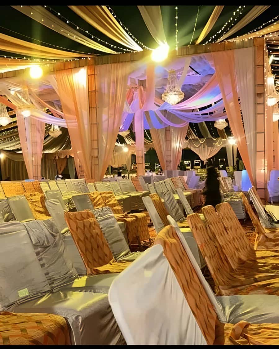 A wedding tent glowing with fairy lights and peach drapes over a lit mandap