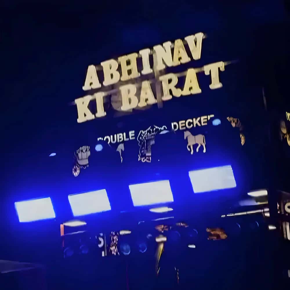 A baraat truck's lit gold sign, Abhinav ki Barat, above glowing blue LED bars at night