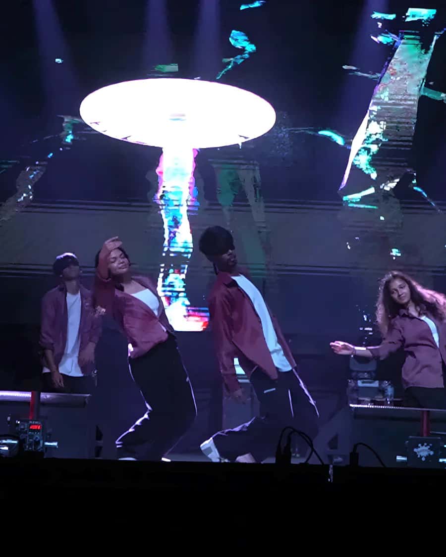 Dancers in maroon shirts on a dark stage under a glowing LED-wall disc at an annual day